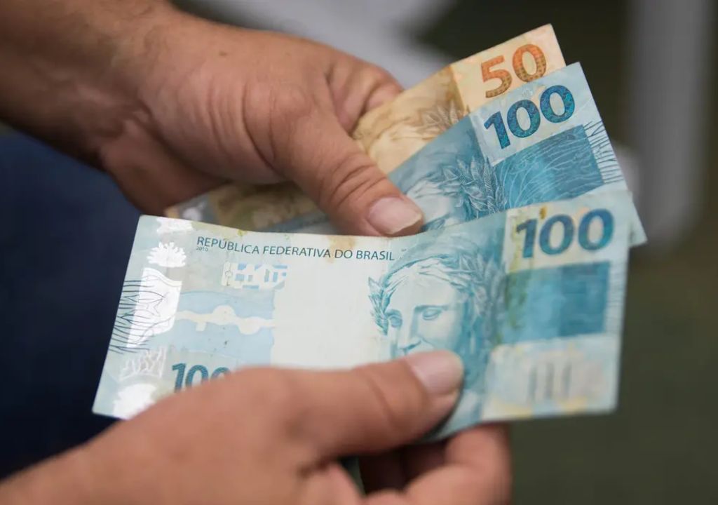 trabalhador consultando abono salarial PIS/Pasep em dispositivo móvel com notas de dinheiro ao fundo