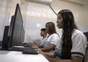 Estudantes utilizam computadores conectados à internet de alta velocidade em ambiente escolar.